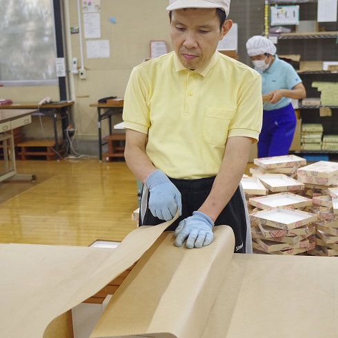 束ねた箱を大きな包装紙で包んでいます